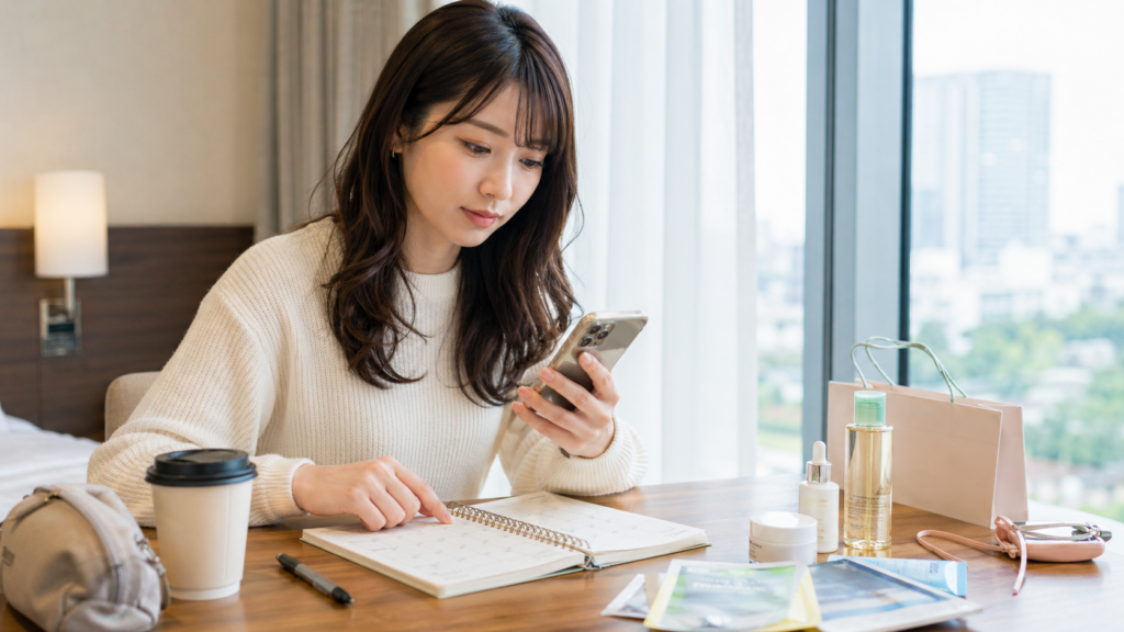 韓国のホテルでスマートフォンと手帳を見ながらオリヤンのセール時期を確認する日本人女性